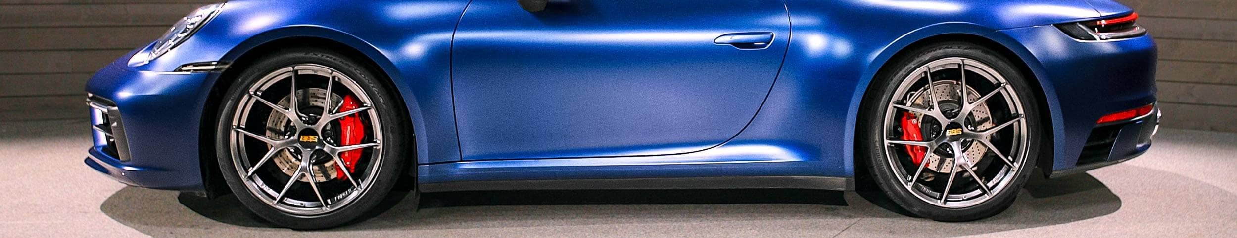 Blue sports car with black rims and red accents on a gray background