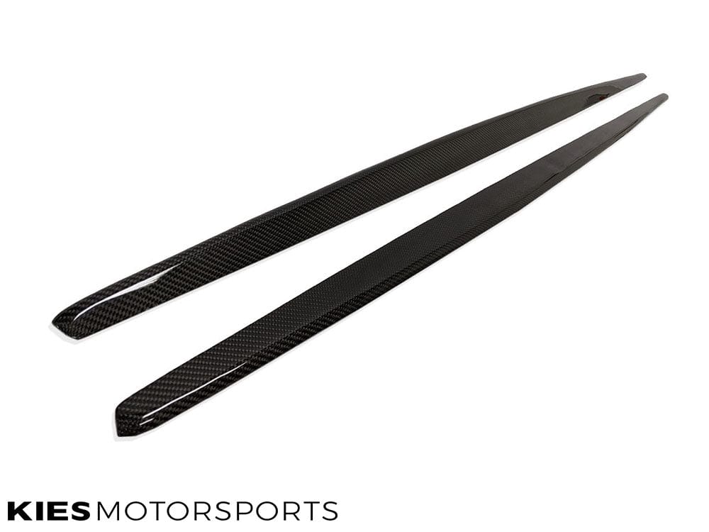Kies Motorsports — pair of carbon fiber side skirt extensions for F22/F23 laid flat, showing gloss finish and carbon weave pattern